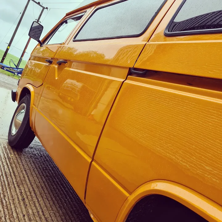 Close view along the glossy side panels and doors of a Volkswagen T25 camper outside the workshop.