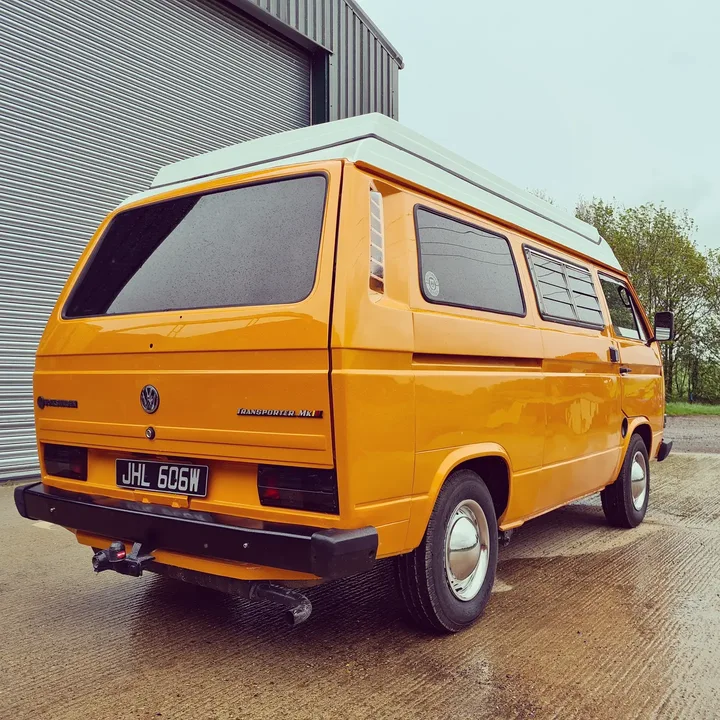 Rear three-quarter view of a Volkswagen T25 camper with a raised roof outside the workshop.