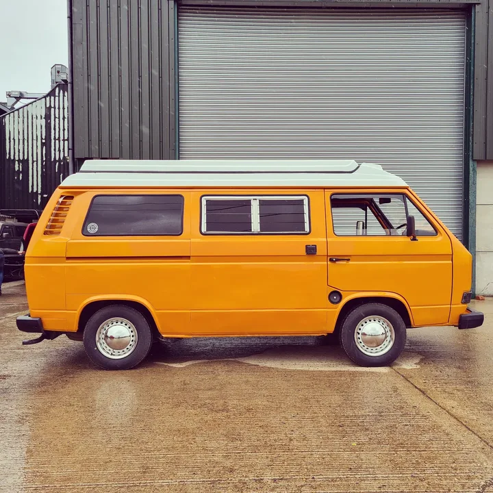 Full side profile of a Volkswagen T25 camper with a raised roof and wheel trims.