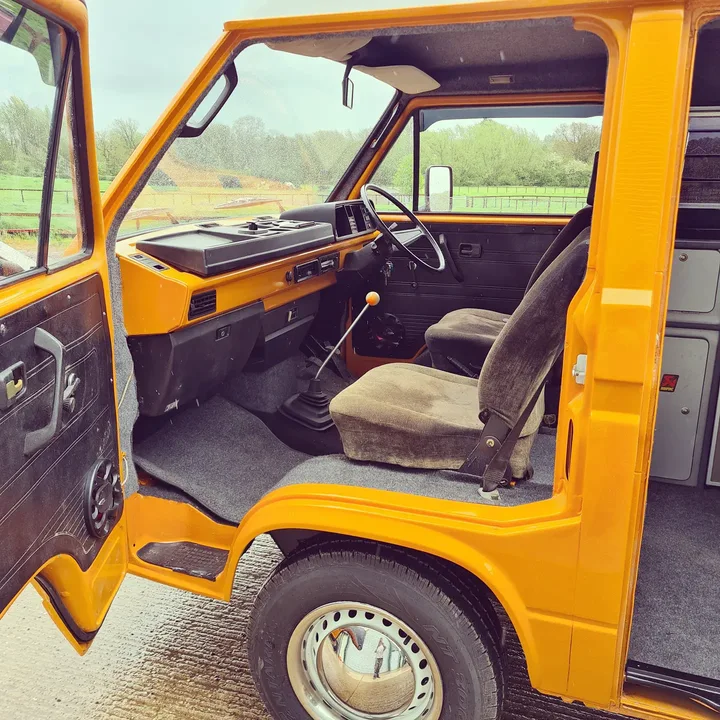 Open front door of a Volkswagen T25 camper showing the seats, dashboard and steering wheel.