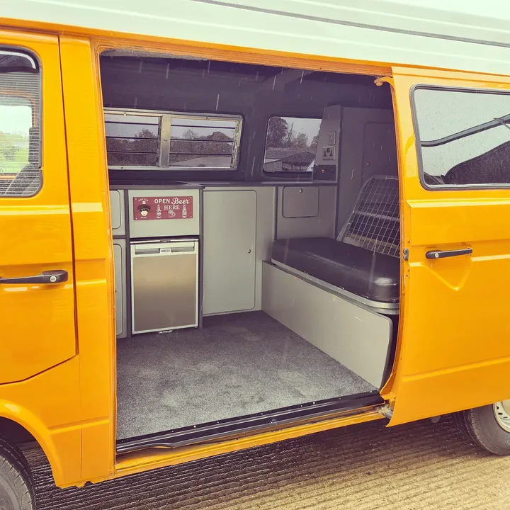 Open sliding door of a Volkswagen T25 camper showing the bench seat and fitted cupboards.