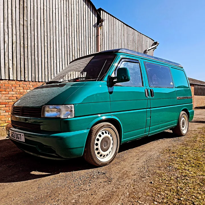 Front three-quarter view of a Volkswagen T4 Transporter with steel wheels beside the workshop building.
