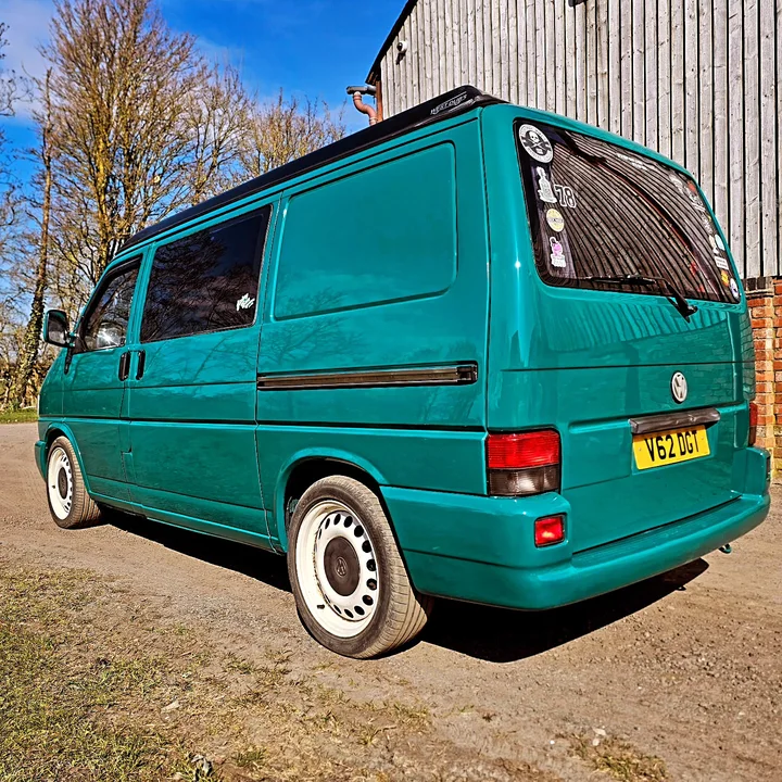 Rear three-quarter view of a Volkswagen T4 Transporter with steel wheels and stickers on the rear window.