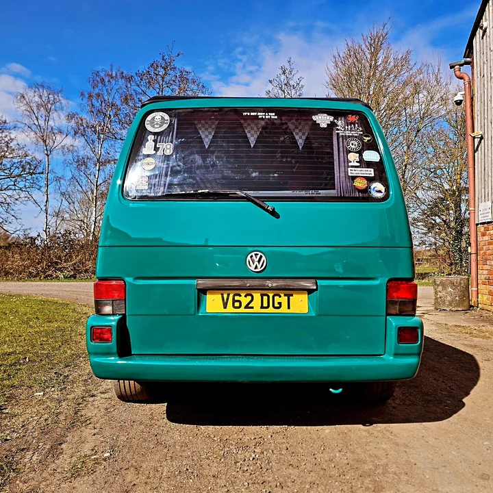 Straight rear view of a Volkswagen T4 Transporter with a stickered rear window, wiper and tail lights.