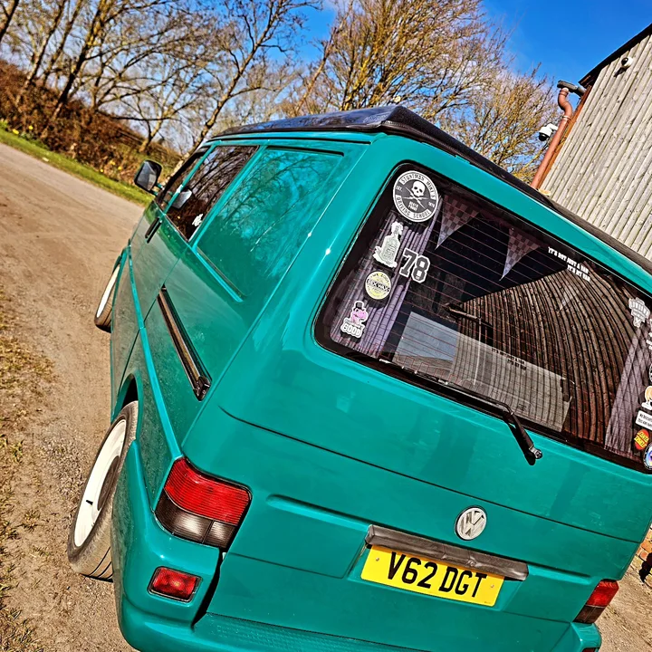 Angled close view of a Volkswagen T4 Transporter rear corner, tailgate and stickered rear window outside the workshop.
