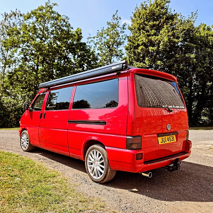 Red T4 Transporter photographed from behind with dark windows, silver wheels and a roof-mounted awning.