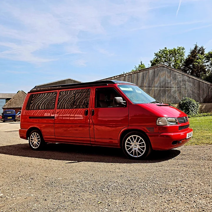 Front three-quarter view of a red T4 Transporter with silver wheels parked outside the workshop.
