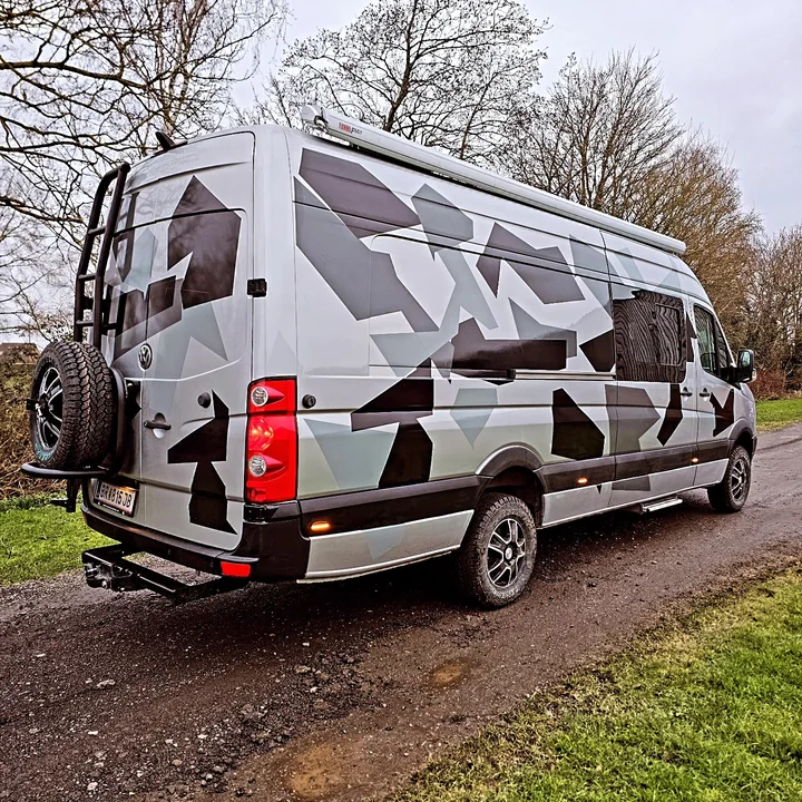 Camouflage-patterned Crafter viewed from behind with rear ladder and external spare wheel.