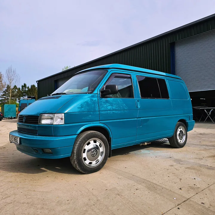 Bright blue Volkswagen T4 Transporter with silver wheel covers parked in front of the workshop.