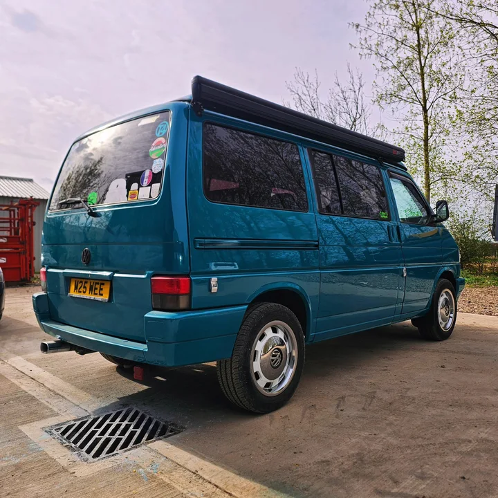 Blue T4 Transporter viewed from the rear with dark side windows and a roof-mounted awning.