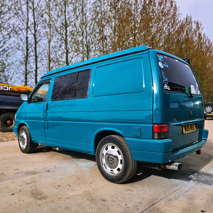 Rear three-quarter view of a blue T4 Transporter with a solid side panel and silver wheel covers.