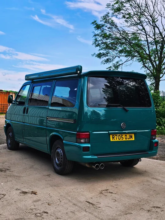 Rear view of a teal T4 Transporter with a roof-mounted awning, dark rear window and twin exhaust outlets.