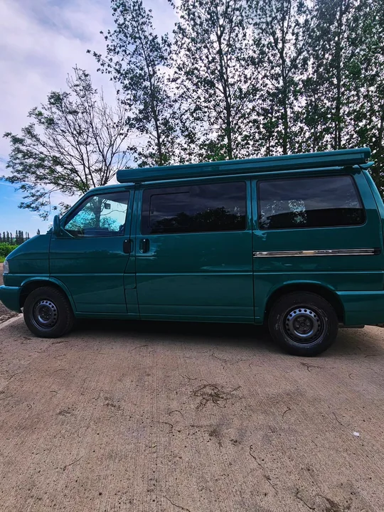 Full side profile of a teal T4 Transporter with dark windows and a roof-mounted awning.