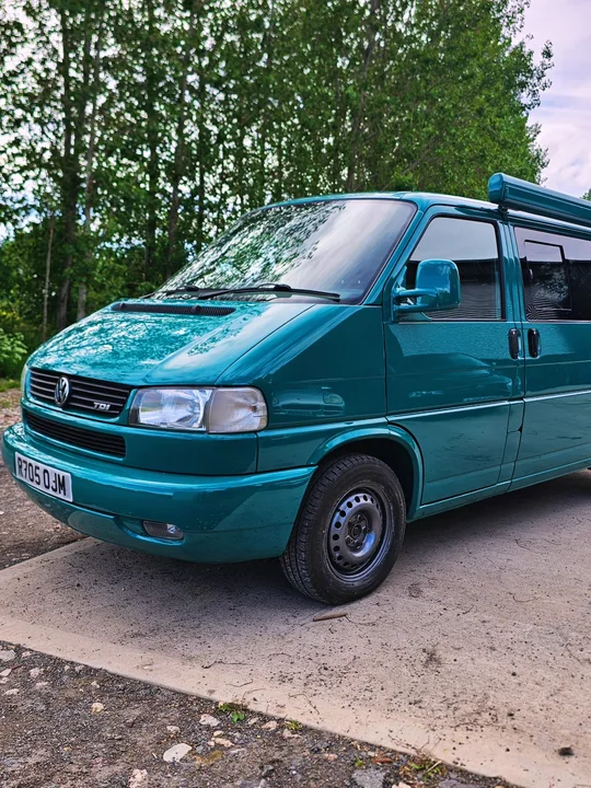 Teal T4 Transporter photographed from the front and side with trees behind it.