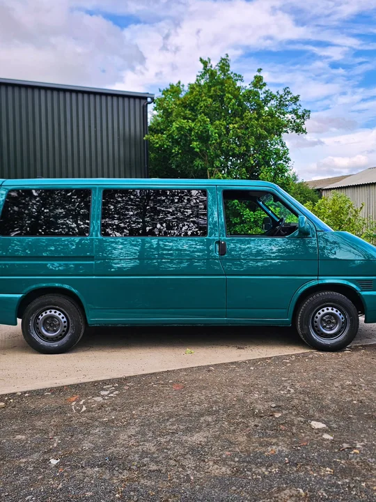 Full side view of a teal T4 Transporter parked outside with dark glass and black wheels.