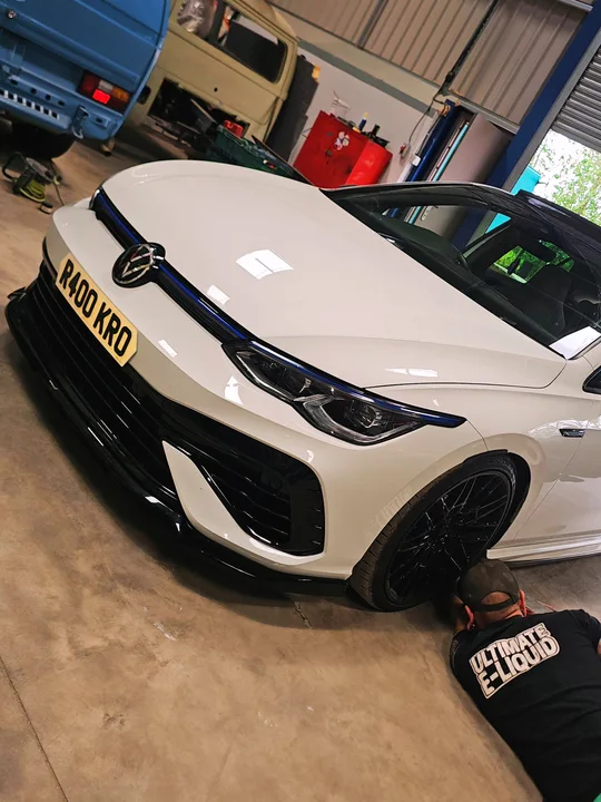 White Volkswagen Mk8 Golf inside the workshop with a person crouching beside the front wheel.