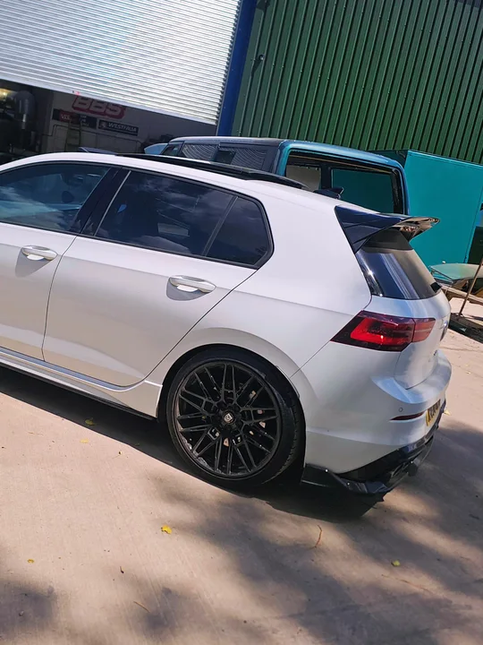 White Volkswagen Mk8 Golf viewed from the rear and side beside the workshop entrance.