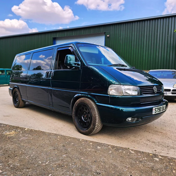 Dark green Volkswagen T4 Transporter with dark windows and black wheels parked outside the workshop.