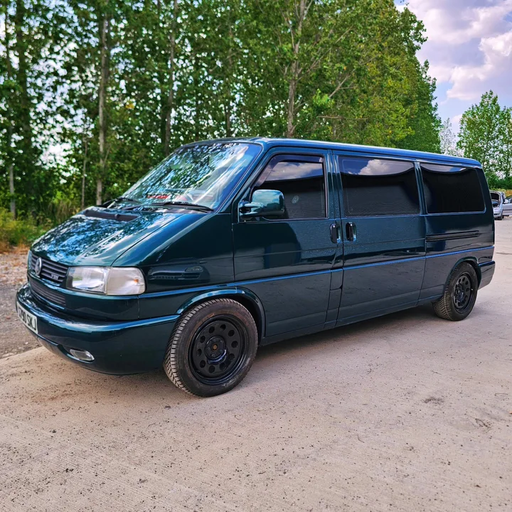 Front three-quarter view of a dark green T4 Transporter with trees behind it.