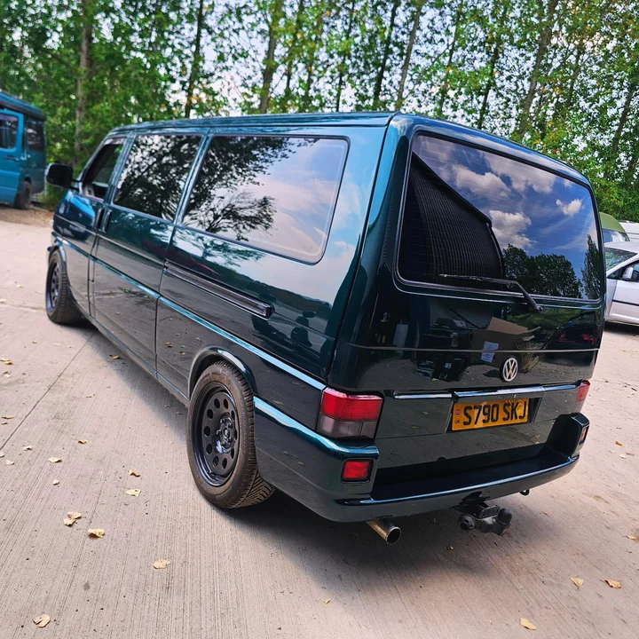 Dark green T4 Transporter rear three-quarter view with dark windows, black wheels and a tow bar.