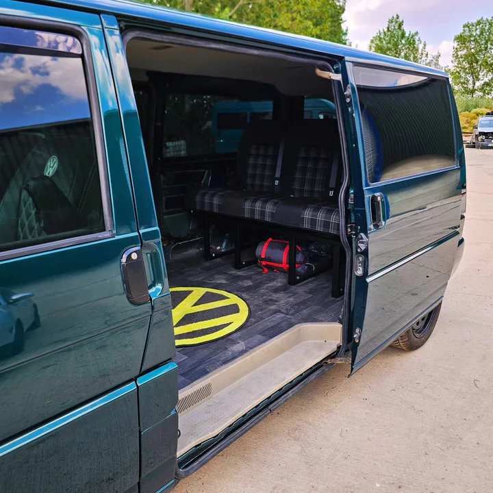 Open sliding door of a dark green T4 Transporter revealing patterned seating and the interior floor.
