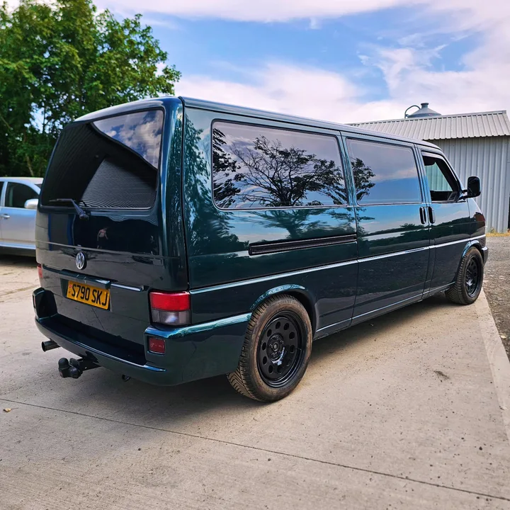 Rear and side view of a dark green T4 Transporter with dark windows and black wheels.