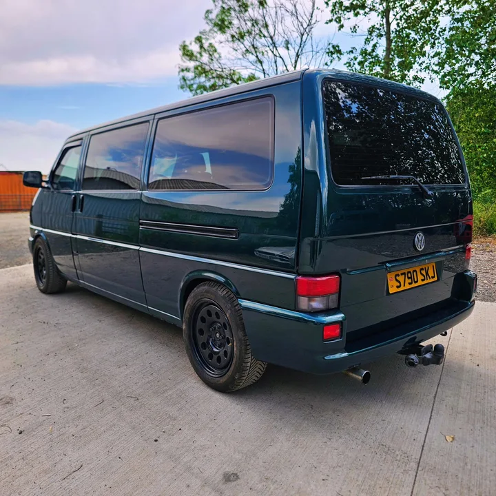 Rear three-quarter view of a dark green T4 Transporter showing its rear window, tail lights and tow bar.