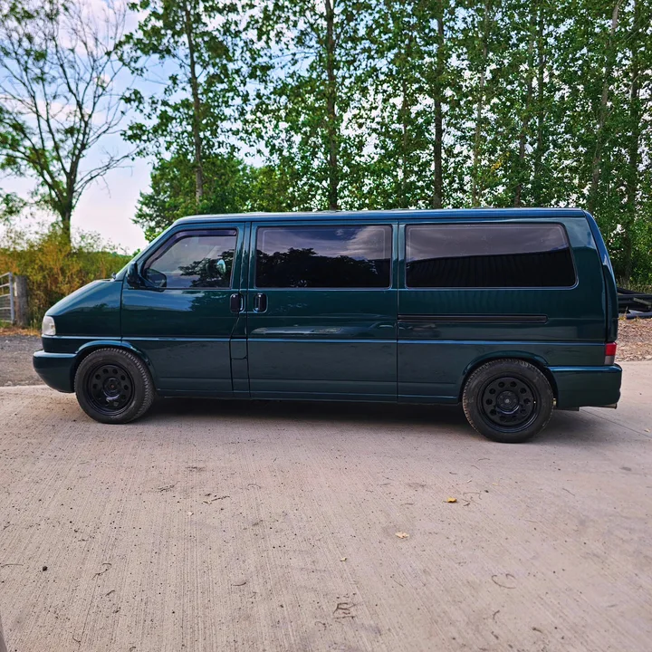 Full side profile of a dark green T4 Transporter with dark side windows and black wheels.
