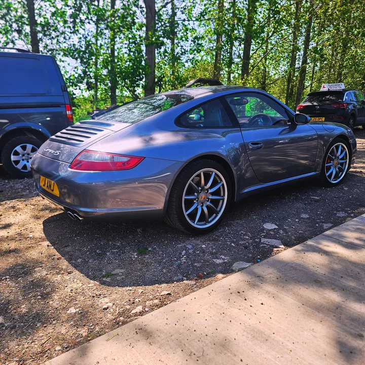 Grey Porsche 911 Carrera S coupe viewed from the rear and side in the workshop yard.