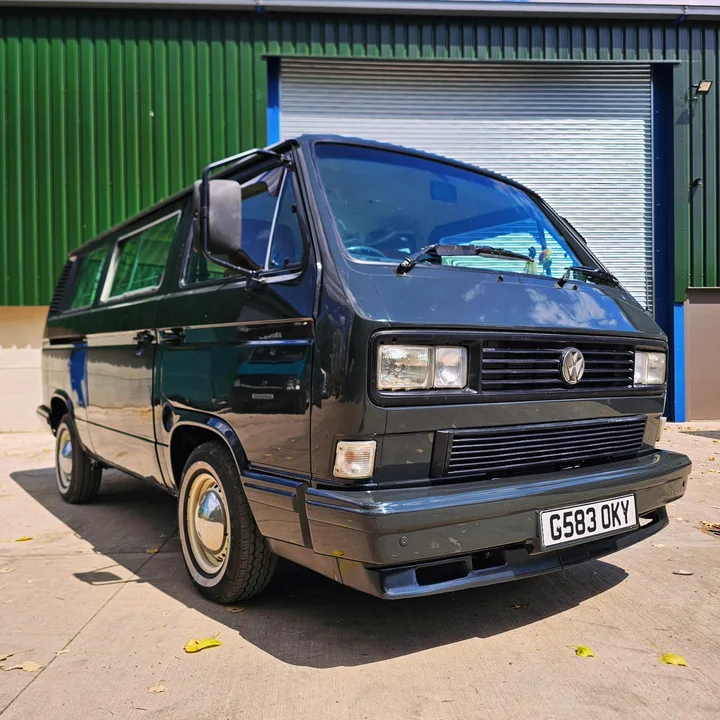 Black Volkswagen T25 camper with rectangular headlights and silver wheel covers outside the workshop.