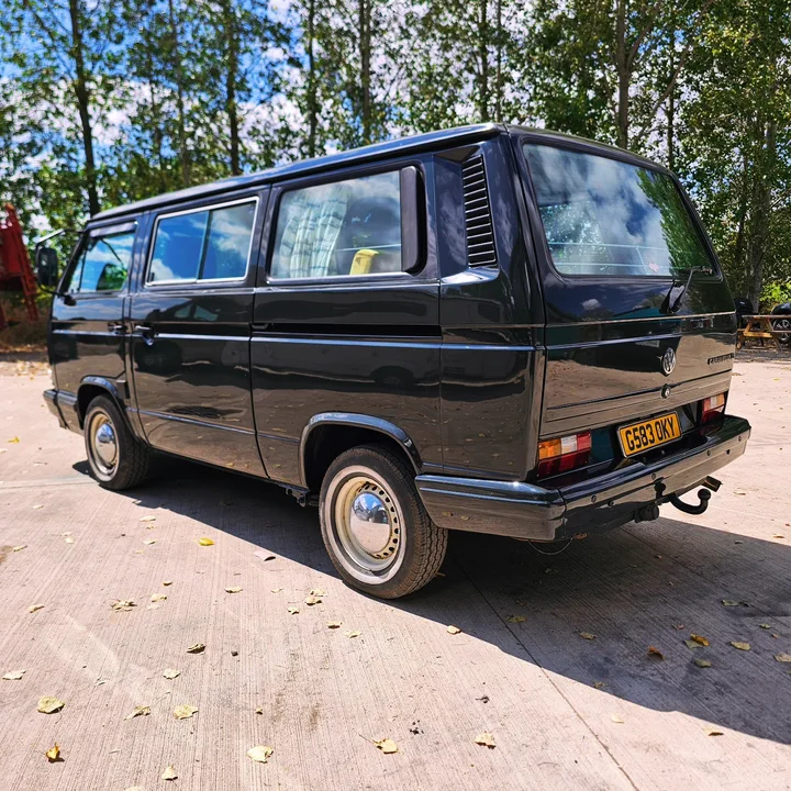 Rear three-quarter view of a black T25 camper showing its side windows, tail lights and tow bar.