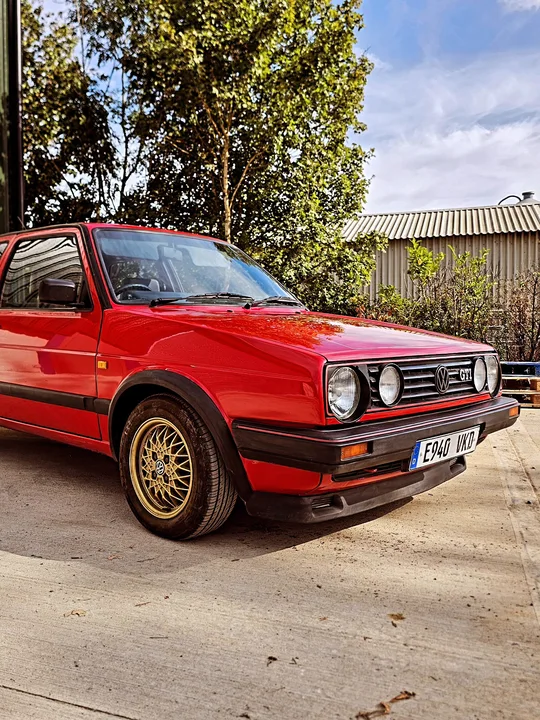 Red Volkswagen Mk2 Golf GTI with gold mesh wheels parked outside the workshop.